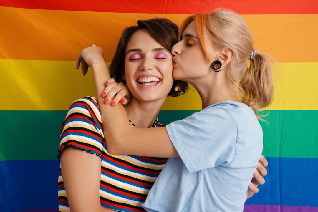 lesbian couple hugging and kissing in front of rainbow